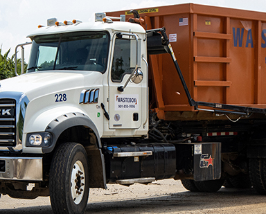 A large white Mack truck hauling an orange dumpster full of refuse.