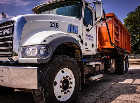 A large semi-truck hauling an orange dumpster.